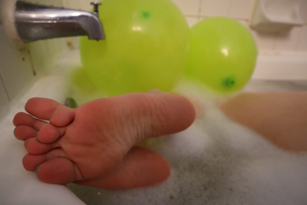 feet in a bathtub with green balloons
